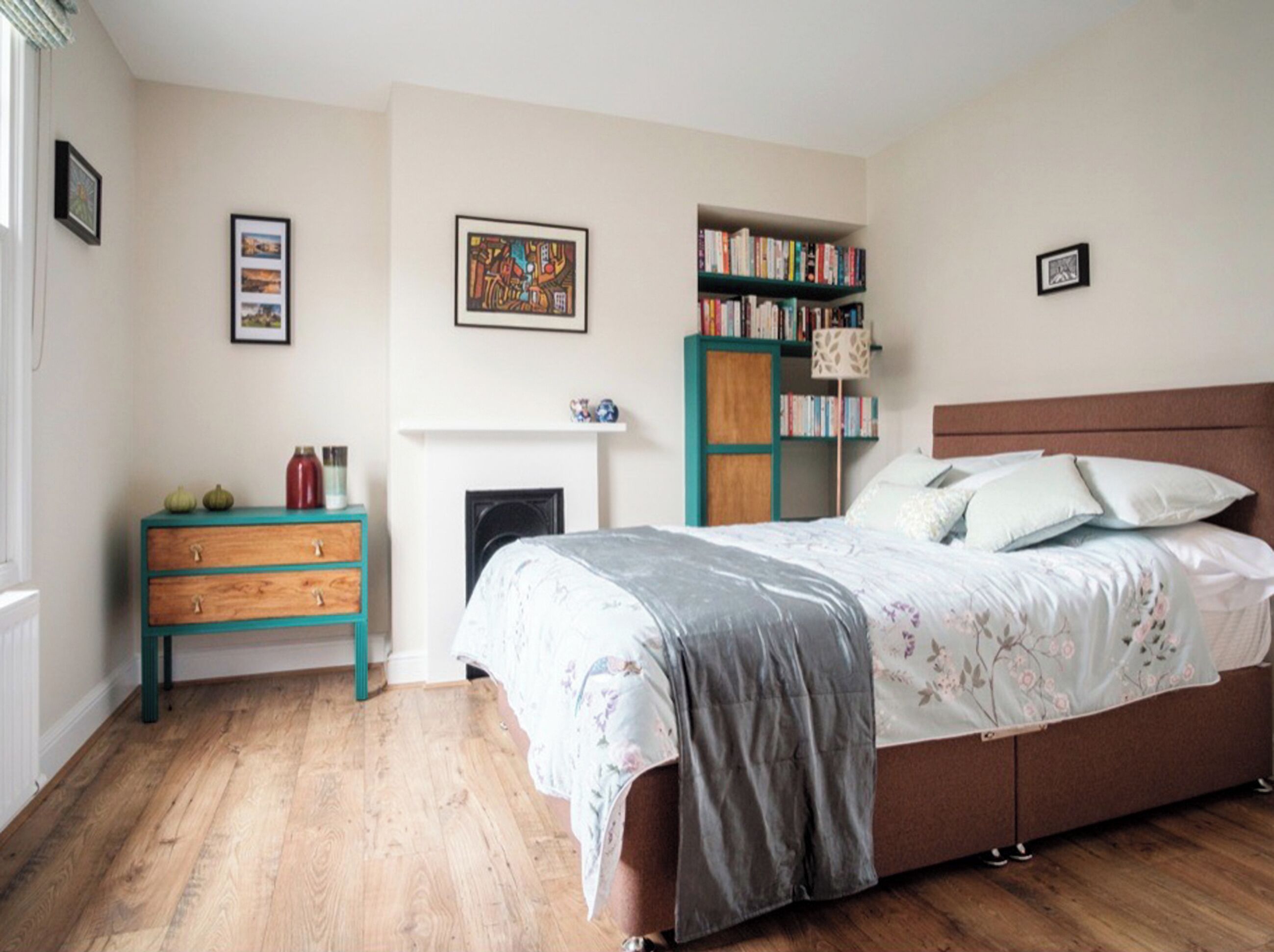 A bedroom with a bed, a dresser, a bookshelf, and a fireplace.