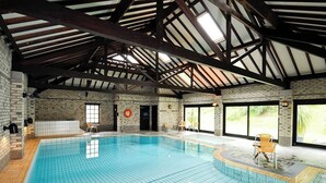 Ein Hallenbad mit gefliestem Boden, Holzbalken, Backsteinwänden und einer Tür mit einem roten, runden Schild.