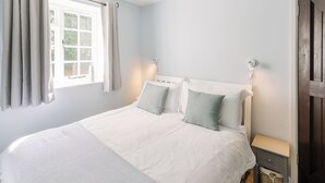 Ein Schlafzimmer mit Bett, Vorhängen, einem Nachttisch und einer Wandleuchte.