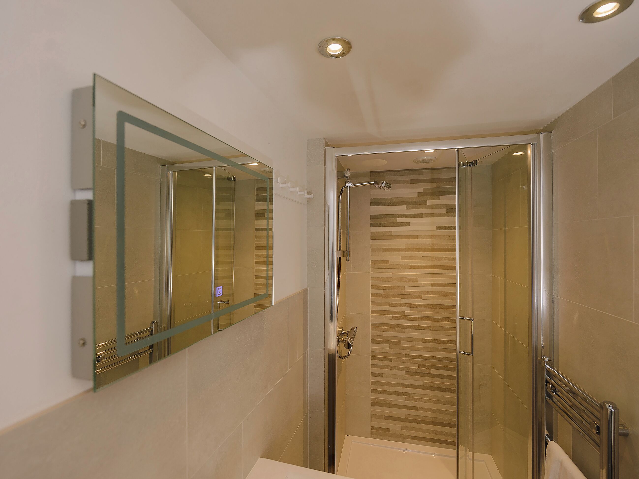 A modern bathroom with a glass shower enclosure, a large mirror, and a tiled floor.