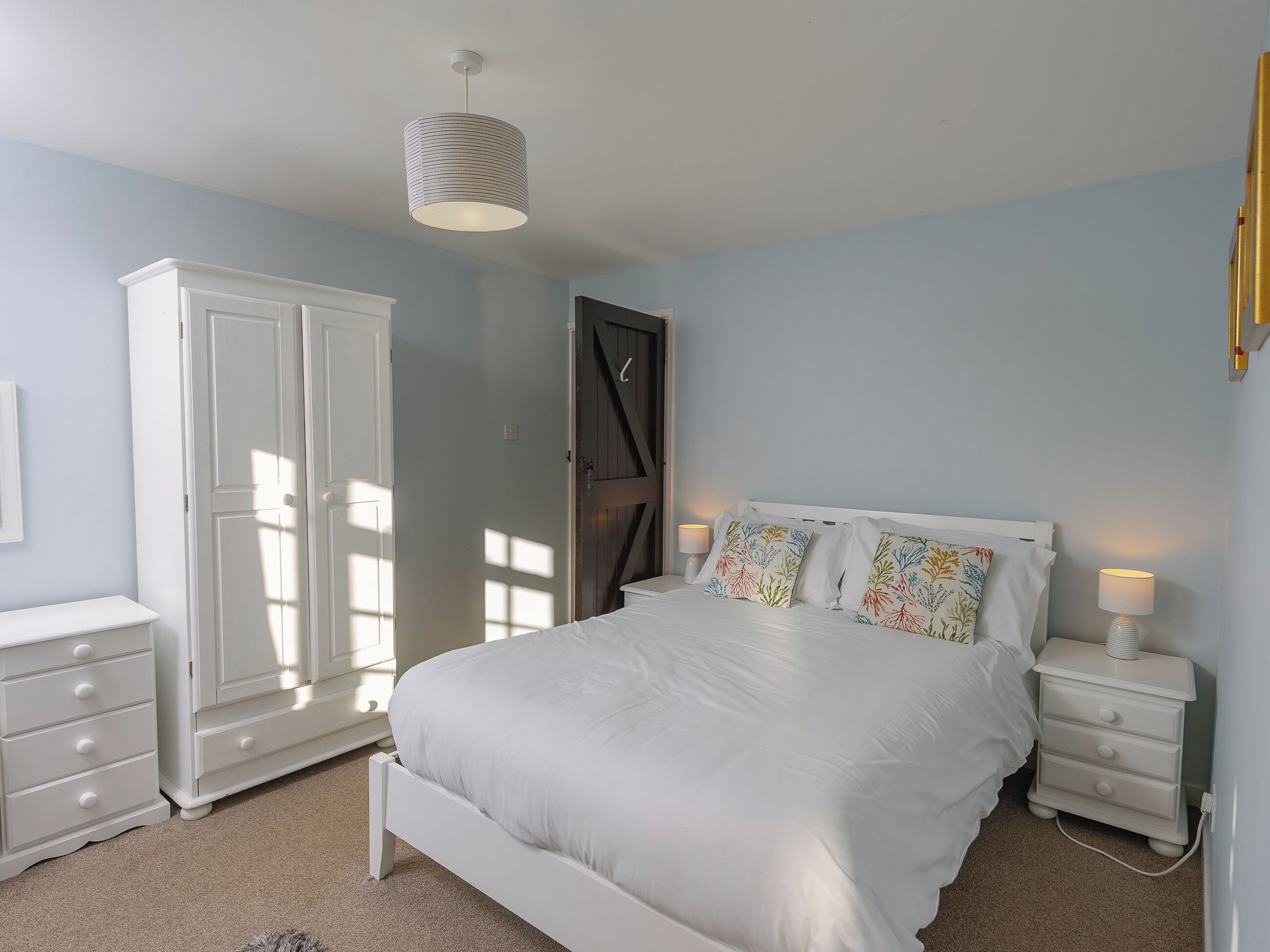 A bedroom with a bed, bedside tables, a wardrobe, and a hanging light fixture.