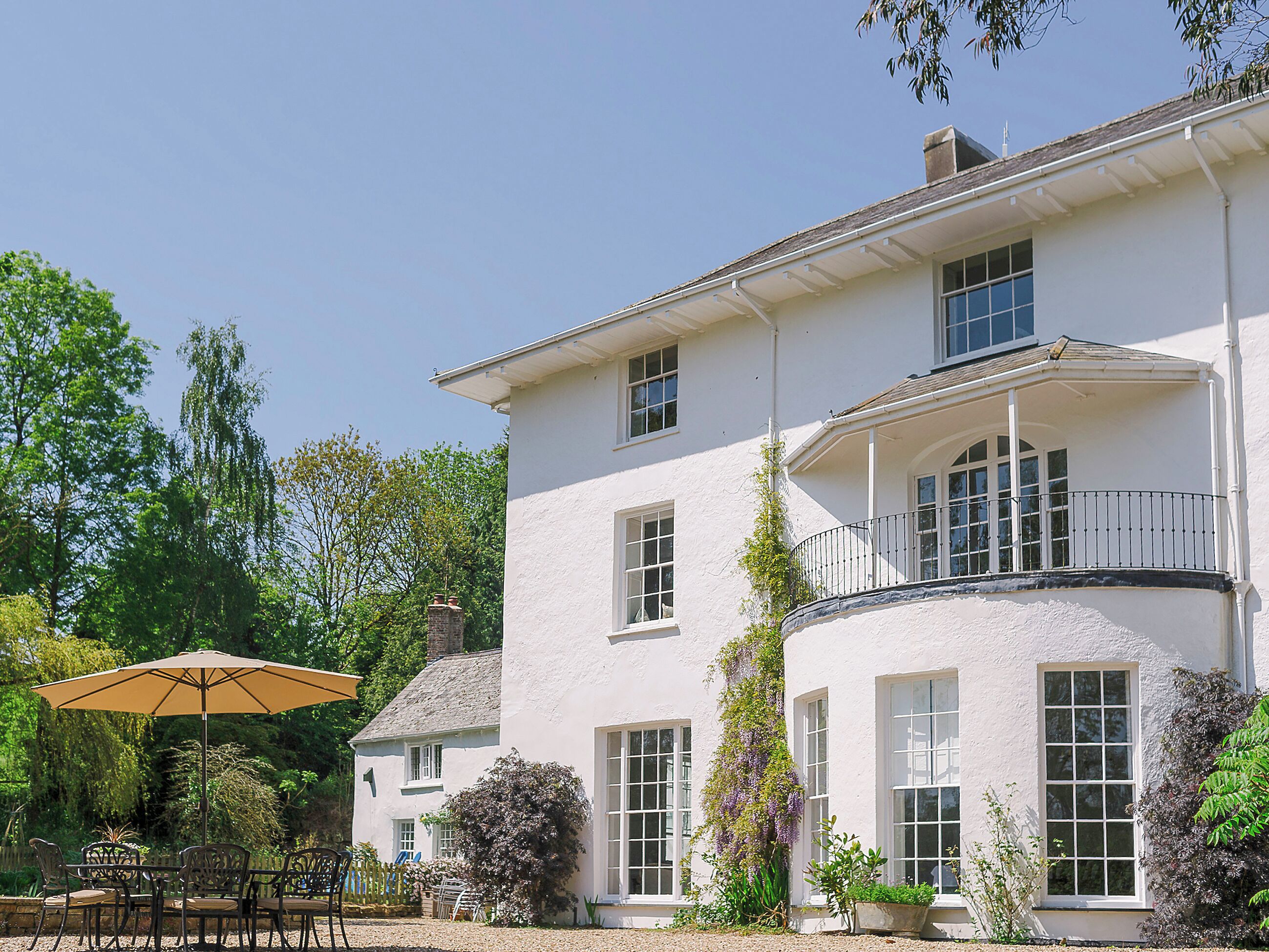 A two-story building with a balcony, large windows, and a patio area with outdoor furniture.
