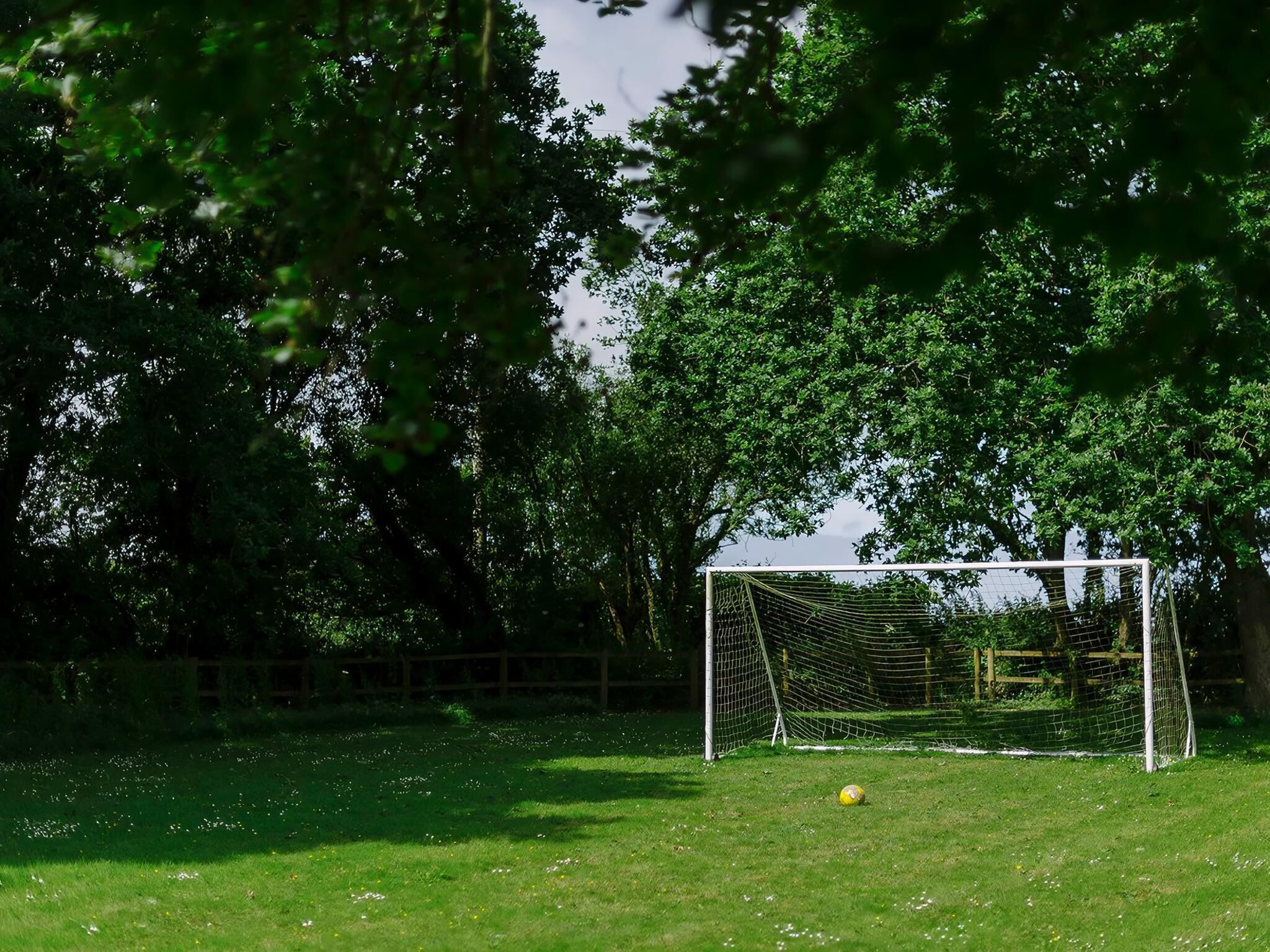 A soccer goal in a grassy field surrounded by trees.