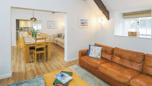 A modern living room with a brown leather sofa, a wooden coffee table with magazines, a dining area with a wooden table and chairs, and a kitchen in the background. - Number Six - UKC4968 (Tawstock, near Barnstaple)