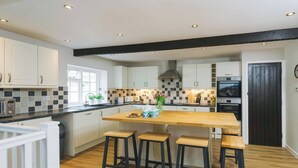 A modern kitchen with white cabinets, a wooden island with stools, a black ceiling beam, and a black door. - Number Six - UKC4968 (Tawstock, near Barnstaple)