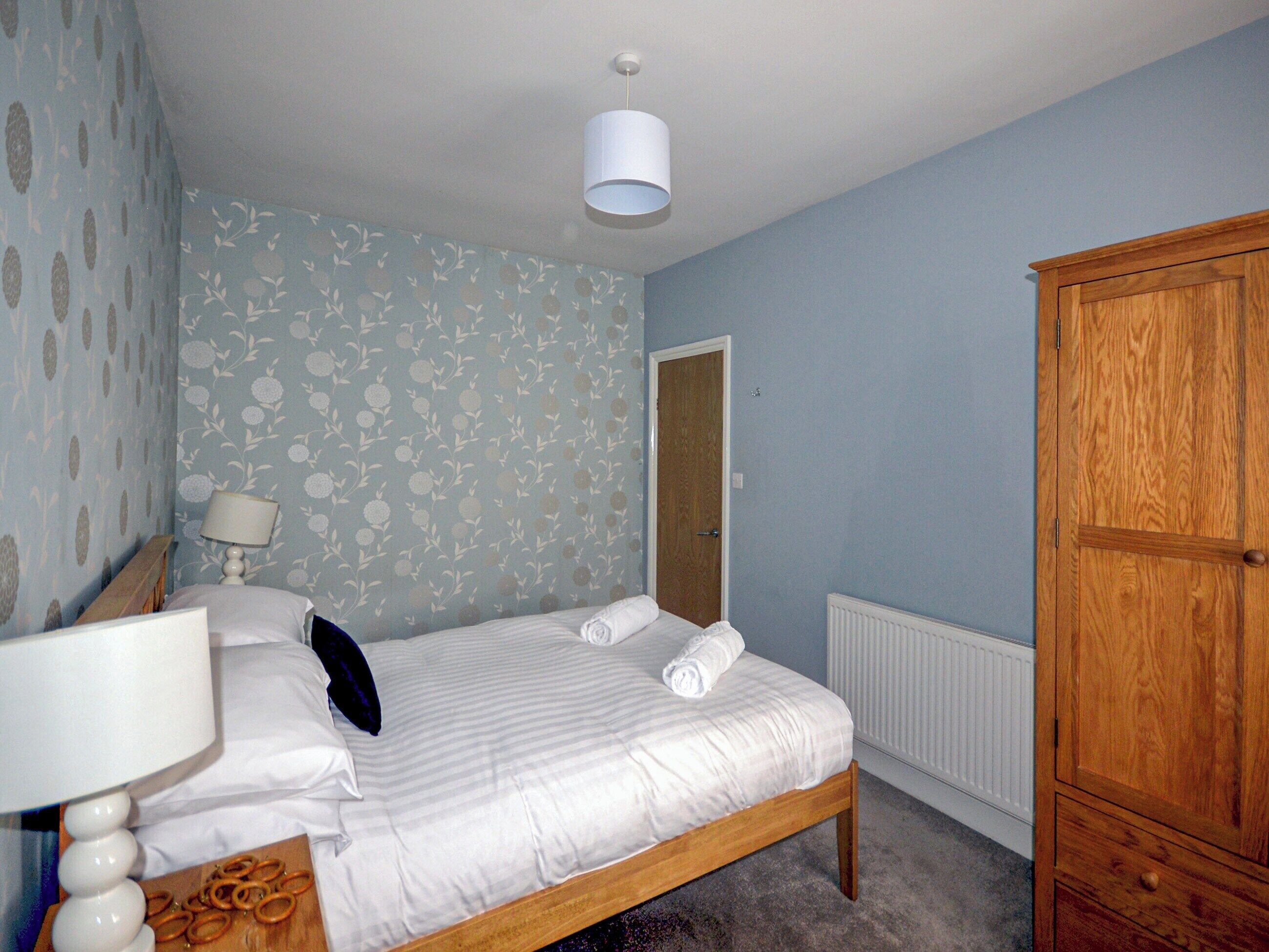 A bedroom with a bed, a wooden wardrobe, a radiator, and a door.
