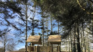 A wooden play structure with climbing walls and slides, surrounded by trees and a stone wall. - Number Four - UKC4966 (Tawstock, near Barnstaple)