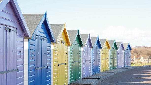 Una fila di casette da spiaggia colorate con tetto spiovente, disposte lungo un vialetto lastricato.