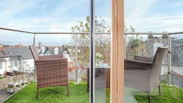 Ein Balkon mit Korbstühlen und Glasgeländer mit Blick auf eine Stadtlandschaft.
