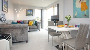 Ein modernes Wohnzimmer mit grauem Sofa, einem Esstisch mit Stühlen und Bildern an den Wänden.