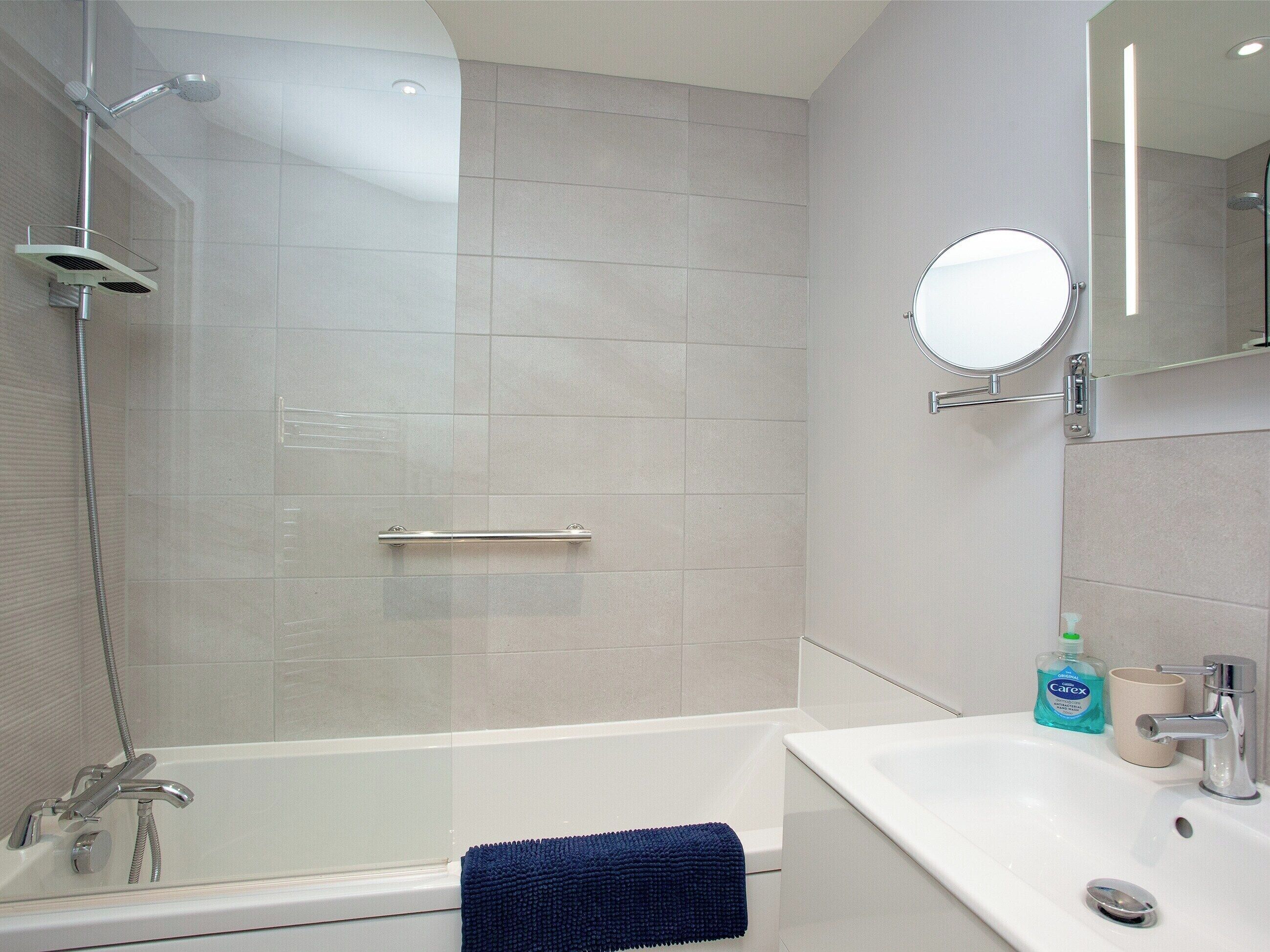 A modern bathroom with a glass-enclosed shower, a white bathtub, a sink, and a mirror.