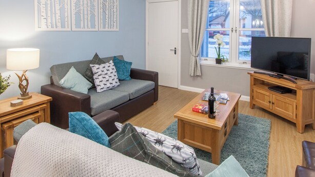 Ein Wohnzimmer mit einer Couch, einem Couchtisch, einem Fernseher und einem Fenster mit Vorhängen.