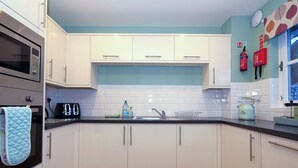 Eine Küche mit weißen Schränken, einem Edelstahlbackofen, einer Spüle und einer türkisblauen Spritzschutzwand.