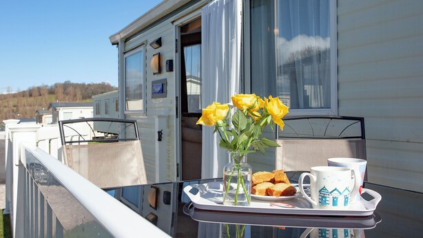 A dining table with a tray of food and drinks, a vase with yellow flowers, and a camper parked in front. - 3 bedroom accommodation in Dawlish Warren (Dawlish Warren)