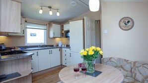 A compact kitchen with a dining area, a microwave, and a clock on the wall. - 3 bedroom accommodation in Dawlish Warren (Dawlish Warren)