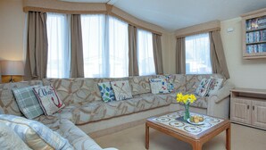 A living room with a sofa, a coffee table with flowers, and a bookshelf. - 3 bedroom accommodation in Dawlish Warren (Dawlish Warren)