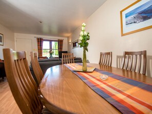 A dining area with a wooden table, chairs, and a vase with flowers. - Munro View - UKC5040 (Aviemore)