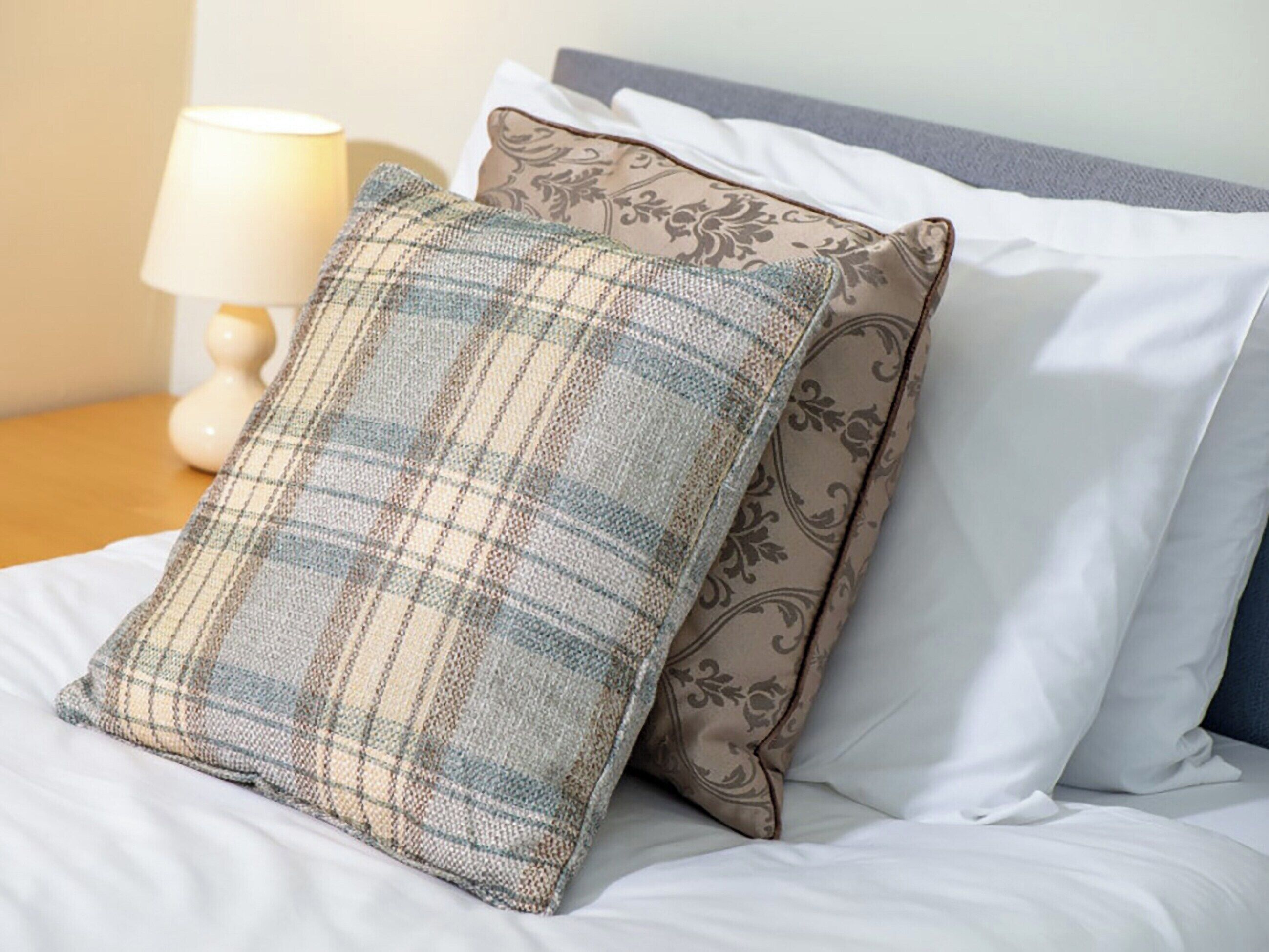A bed with white sheets and two decorative pillows, one with a plaid pattern and the other with a floral design.