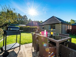 Eine Terrasse mit Grill, Korbmöbeln und einer Weinflasche.