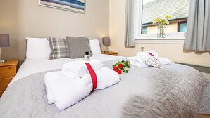 A hotel room with a large bed, a bedside table, a nightstand, a window with curtains, and a painting on the wall. - 3 bedroom accommodation in Aviemore (Aviemore)