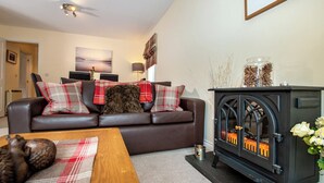 A cozy living room with a brown leather sofa, plaid cushions, a wooden coffee table, and a black wood-burning stove. - 3 bedroom accommodation in Aviemore (Aviemore)