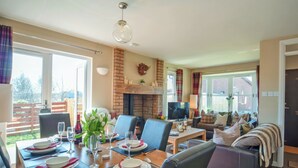 Een eethoek met een houten tafel gedekt voor vier personen, een open haard en een zithoek met een bank en televisie.