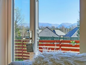 Una habitación con un ventanal grande, una puerta de madera y vistas a un patio cercado con casas y montañas al fondo.