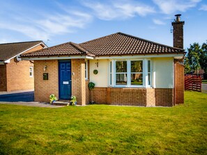A single-story house with a brick facade, a dark blue front door, and a small front yard with grass and two potted plants. - Applewood Cottage - UKC5047 (Aviemore)