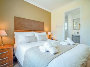 A neatly made bed with white linens and pillows, a bedside table with a lamp, and a bathroom visible through an open door. - Birchdale Cottage - UKC5049 (Aviemore)