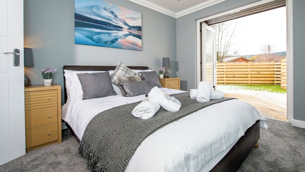 A bedroom with a large bed, two bedside tables, a nightstand, a painting, and a view of the outdoors. - 1 bedroom accommodation in Aviemore (Aviemore)