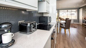 A modern kitchen with a Bosch coffee maker, a toaster, and a stove. There is a dining area with a table and chairs visible in the background. - 1 bedroom accommodation in Aviemore (Aviemore)