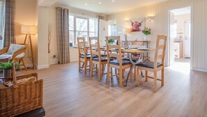 A spacious dining area with a wooden table and chairs, a large window with curtains, and a modern kitchen visible through an open door. - Eagle 3 Star - UKC5056 (Aviemore)