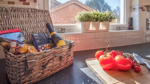 A kitchen with a wicker basket containing groceries, a cutting board with tomatoes, and a window with a view of a house and trees. - Eagle 3 Star - UKC5056 (Aviemore)