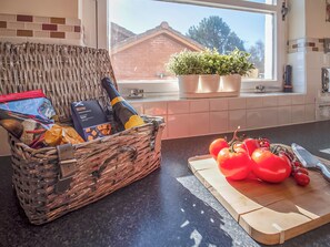 A kitchen with a wicker basket containing groceries, a cutting board with tomatoes, and a window with a view of a house and trees. - Eagle 3 Star - UKC5056 (Aviemore)