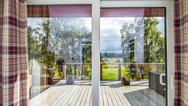 Eine Holzterrasse mit einer Glastür, die auf eine grüne Landschaft blickt.