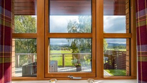 Ein Fenster mit Blick auf eine grüne Landschaft und eine Holzterrasse.
