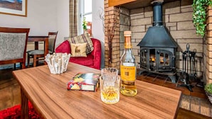 Ein gemütliches Wohnzimmer mit Kamin, einem roten Sofa, einem Holztisch mit Gläsern und einer Flasche Alkohol sowie einem Bücherregal.