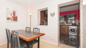 A dining area with a table and chairs, a kitchen with a washing machine, and a window with a view of a building. - Larrach Beag-UKC5059 (Aviemore)