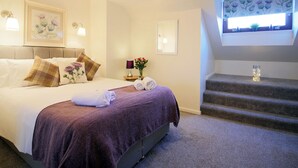 A hotel room with a bed, a nightstand, a mirror, a window with curtains, and a staircase. - Ruby Cottage-UKC5064 (Aviemore)