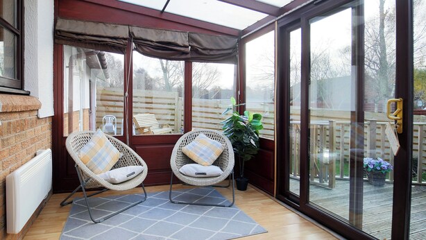 A sunroom with two wicker chairs, a grey rug, and a view of the backyard through large glass doors. - Ruby Cottage-UKC5064 (Aviemore)