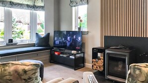 Ett vardagsrum med en tv, en öppen spis och ett fönster med gardiner.