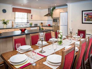 A dining area with a long table set for a meal, surrounded by chairs. - Golden Eagle-UKC5057 (Aviemore)