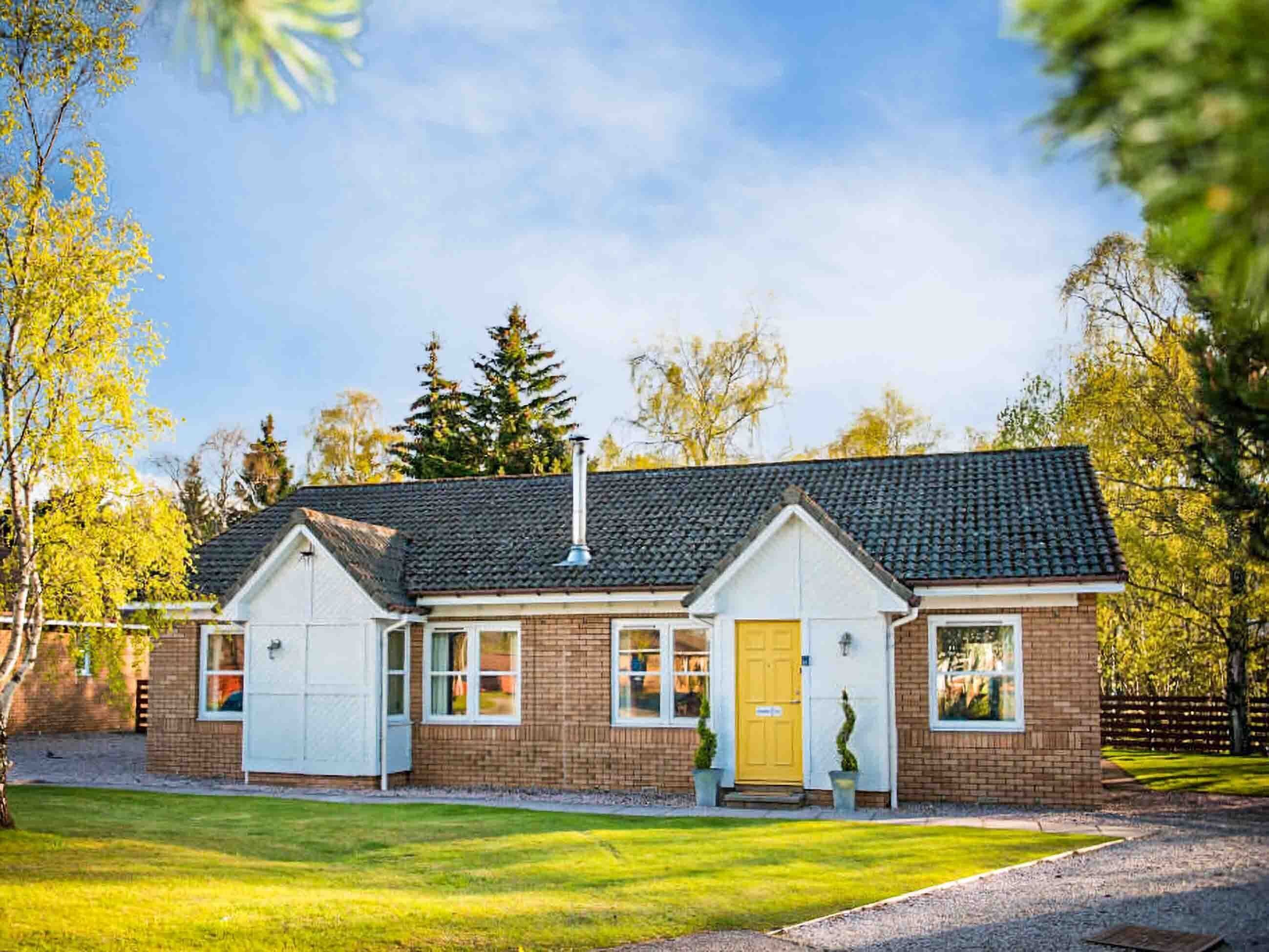 Een tweelaags huis met een bakstenen gevel, pannendak en voortuin met gazon en houten hek.