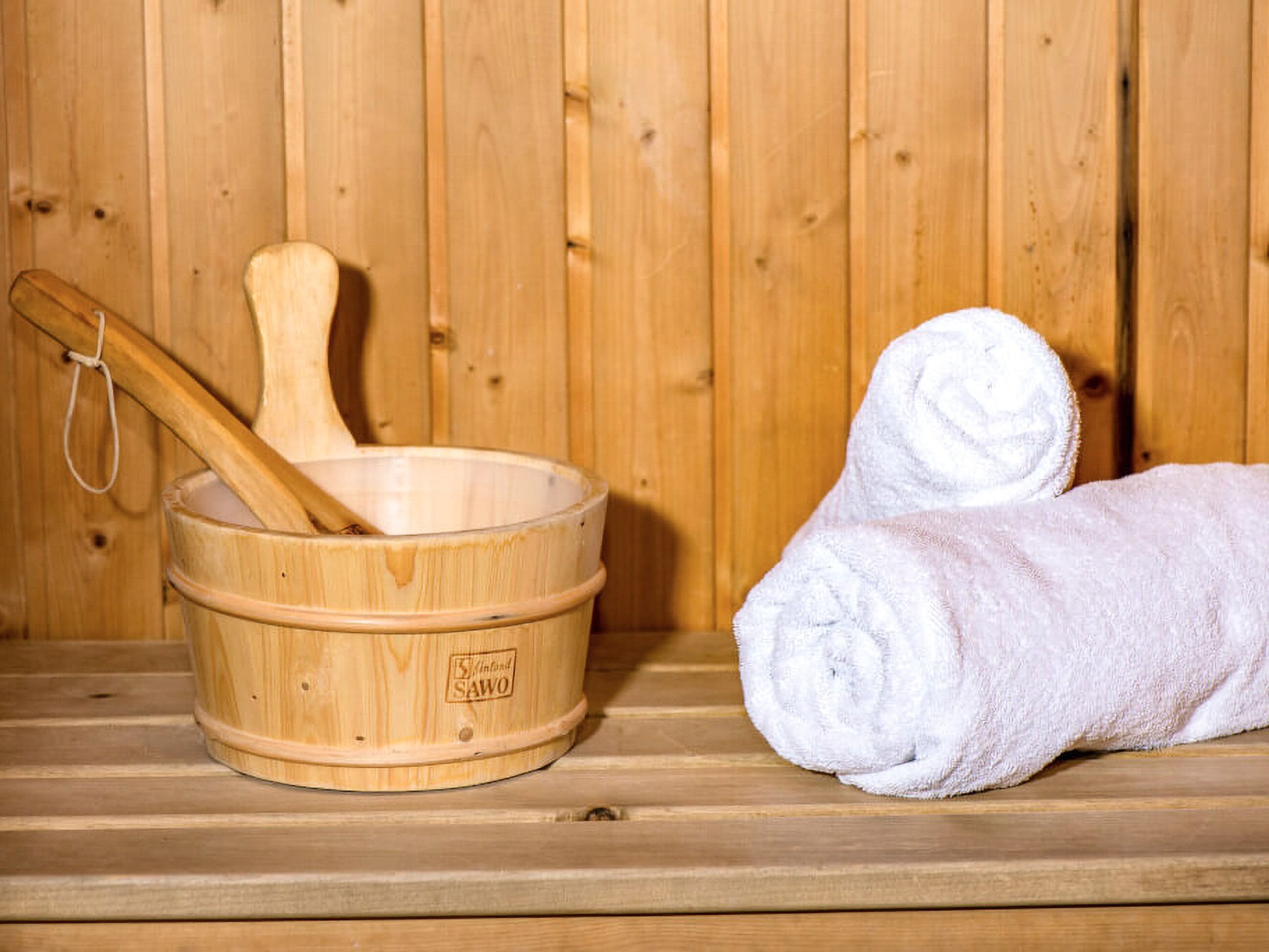Una sauna de madera con una tina de madera y una cuchara de servir. Hay dos toallas enrolladas junto a la tina.