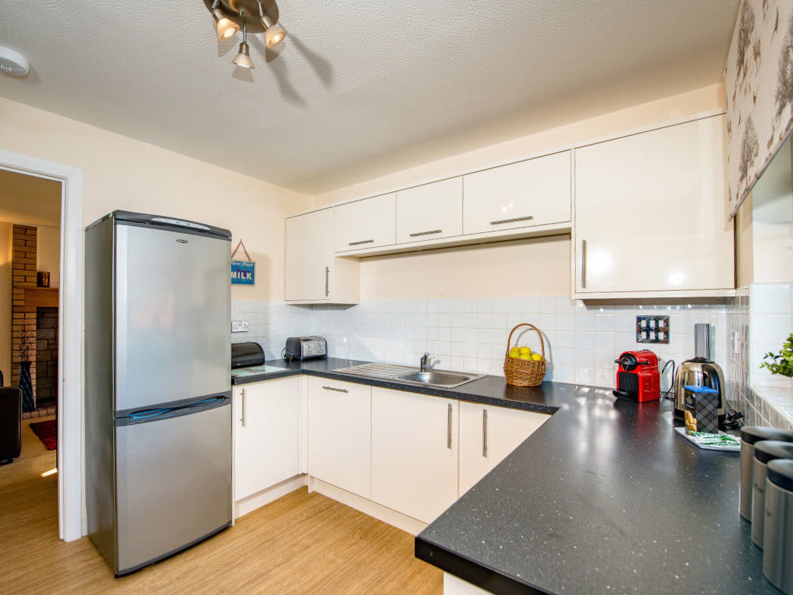 A modern kitchen with white cabinets, a stainless steel refrigerator, a black countertop, and a ceiling fan.