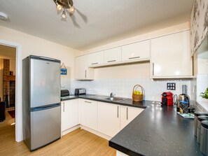 A modern kitchen with white cabinets, a stainless steel refrigerator, a black countertop, and a ceiling fan. - 3 bedroom accommodation in Aviemore (Aviemore)