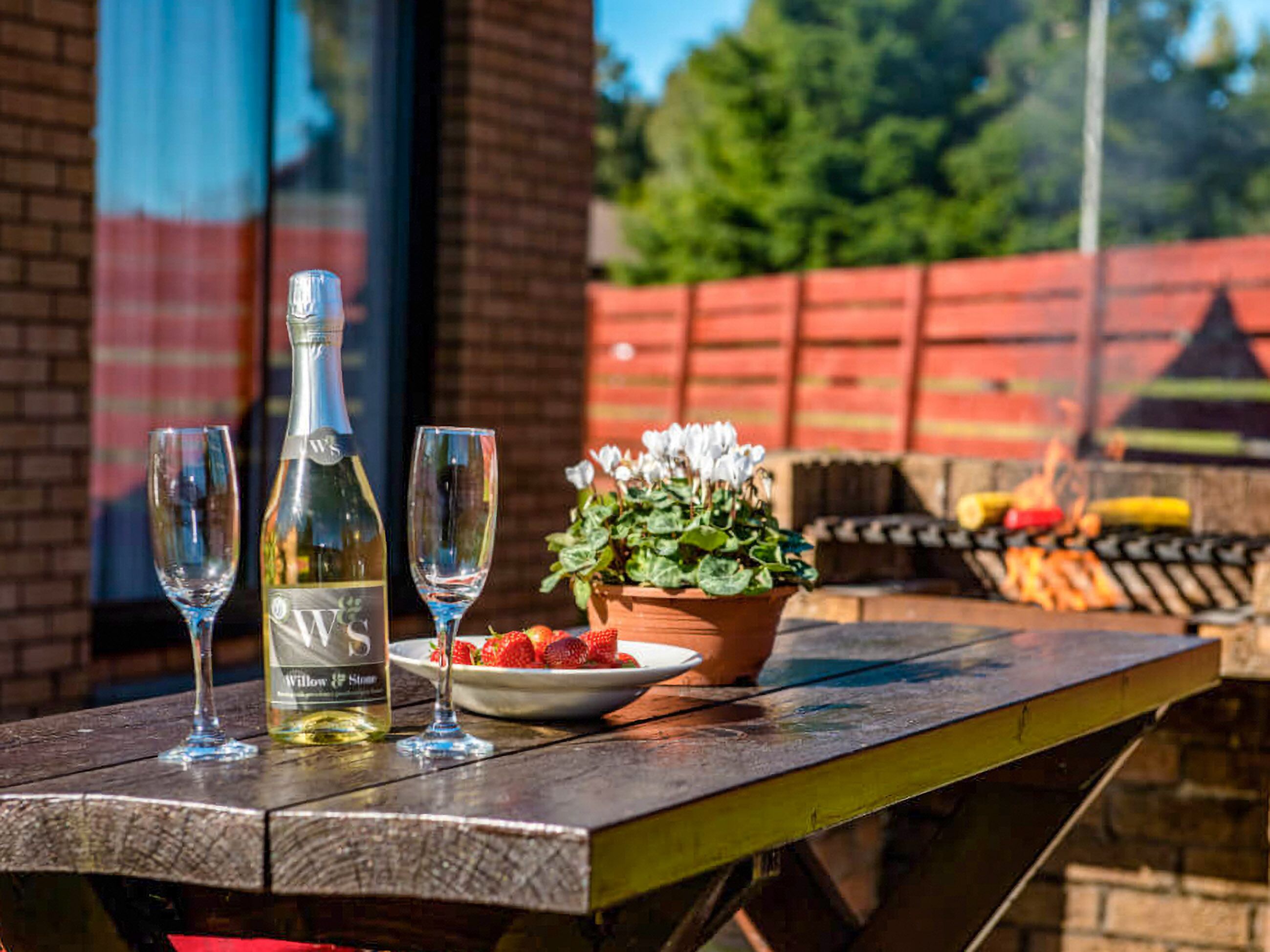 A wooden table with a bottle of white wine, two glasses, a plate of strawberries, and a potted plant.