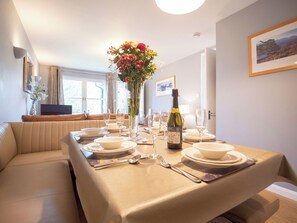 A dining area with a table set for four, a vase of flowers, and a bottle of wine. - 2 bedroom accommodation in Aviemore (Aviemore)