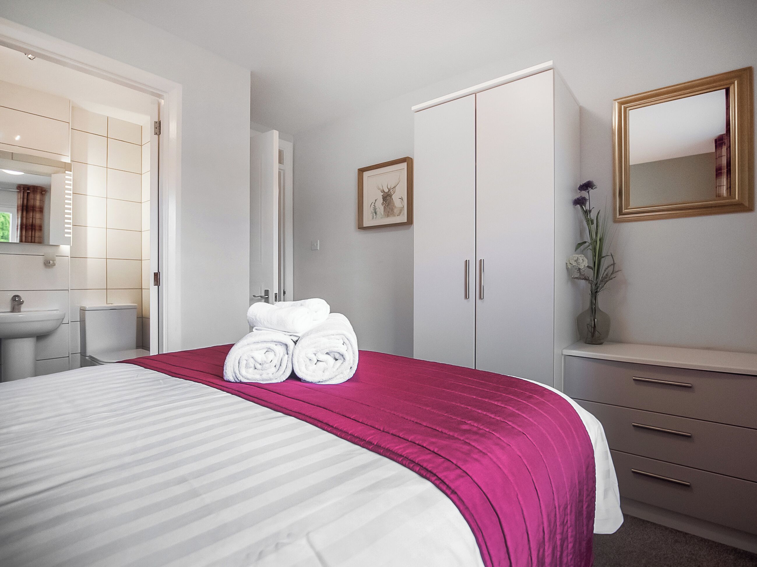A hotel room with a bed, a wardrobe, a mirror, a sink, and a framed picture on the wall.