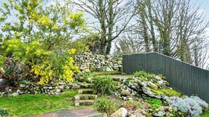 Un jardín con una escalera de piedra, una valla de madera y diversas plantas.